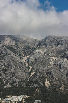 Dramatic Mountain Peaks With Swirling Clouds Above White Mediterranean Village In Greece