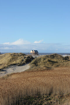 German North Sea Coast Beach With Iconic Stilt Houses And Couple Walking Through Dunes