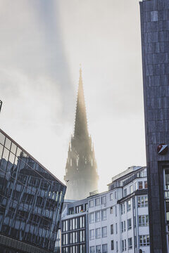 Gothic Church Spire Emerging From Morning Mist Framed By Modern Buildings With Bird In Flight