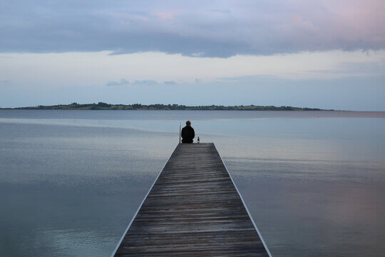 Solitary Figure At End Of Wooden Pier Contemplating Sunset With Wine Bottle