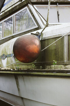 Weathered Houseboat Hull With Copper Buoy Covered In Moss And Algae