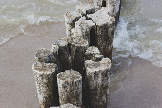 Weathered Wooden Groynes Extending Into Sea On Sandy Beach